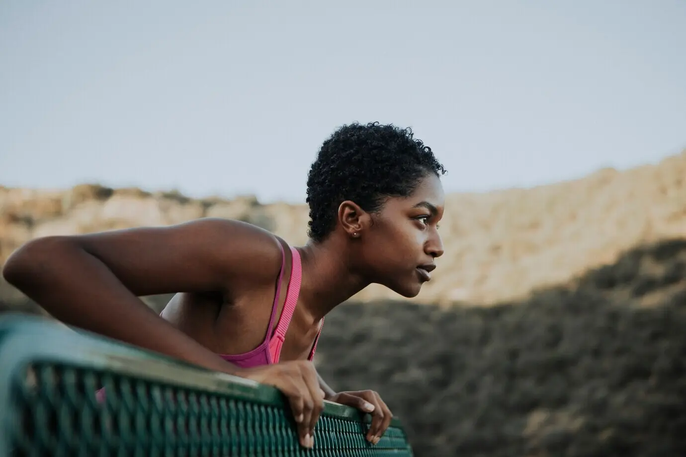 A woman stretches against a park bench.